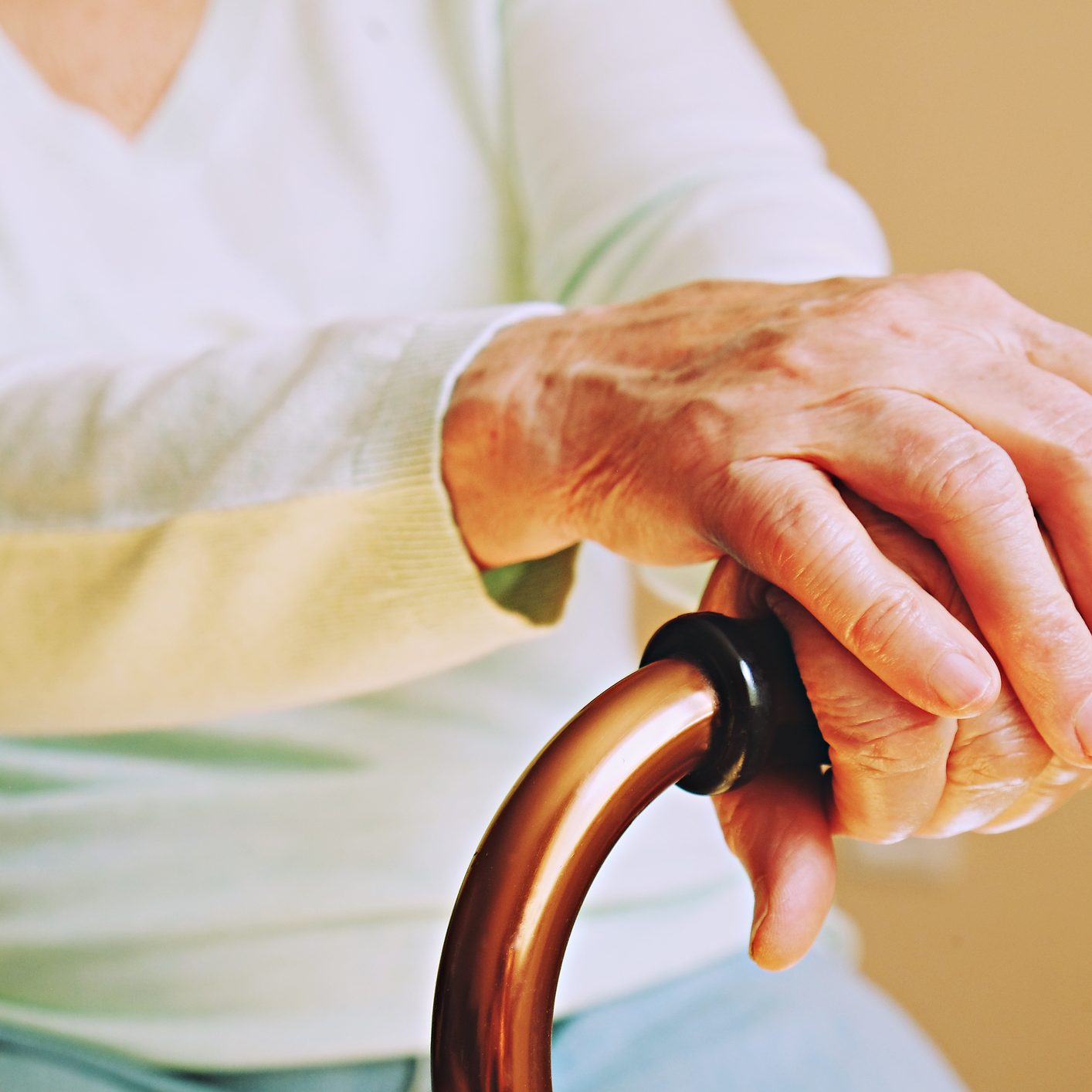 Mature female in elderly care facility gets help from hospital personnel nurse. Close up of aged wrinkled hands of senior woman. Grand mother everyday life. Elderly woman in nursing home, wrinkled hand with clearly visible veins holding walking quad cane. Old age senior lady arms with freckles lay on aid stick handle bar. Background, close up, copy space.