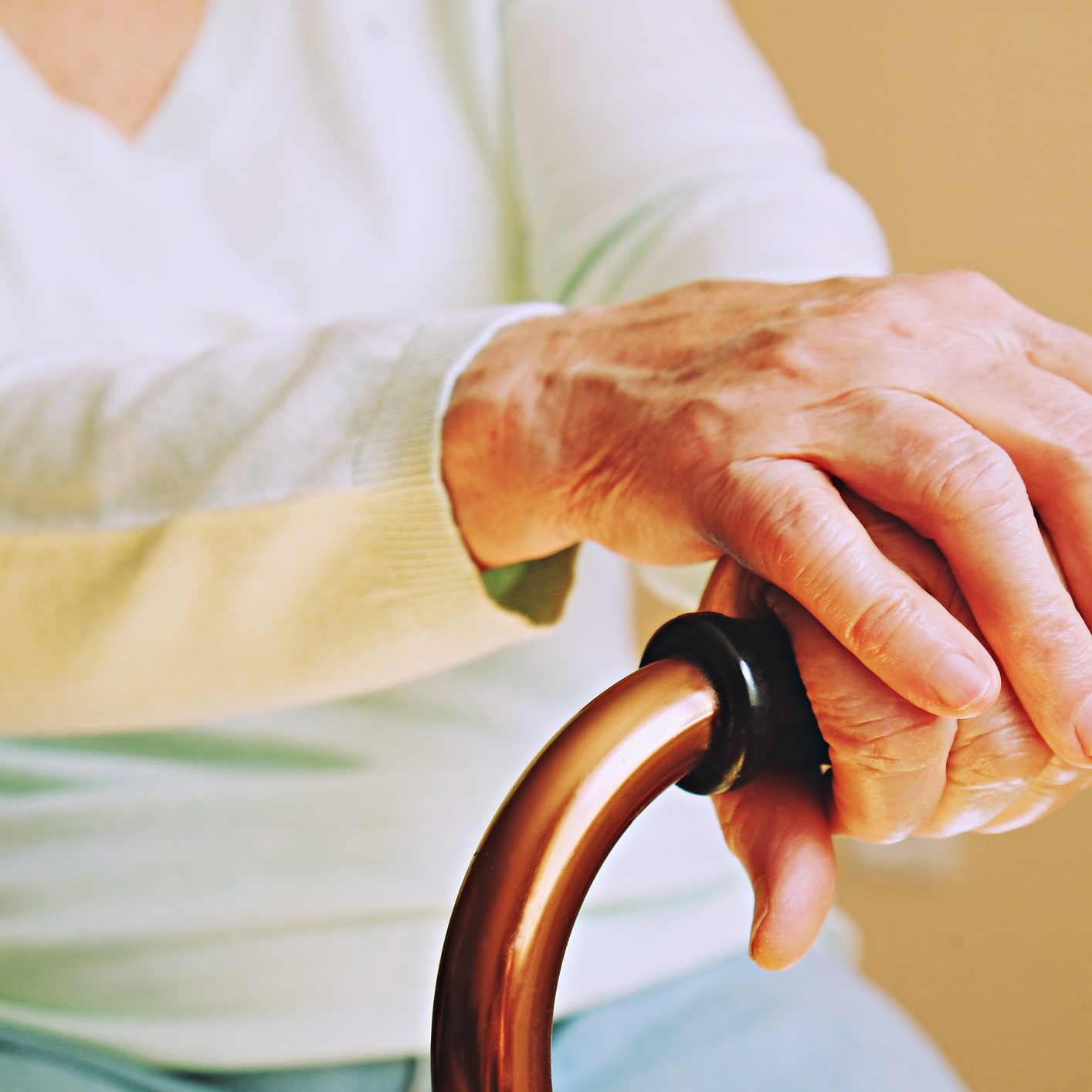 Elderly woman in nursing home, wrinkled hand with clearly visible veins holding walking quad cane. Old age senior lady arms with freckles lay on aid stick handle bar. Background, close up, copy space.